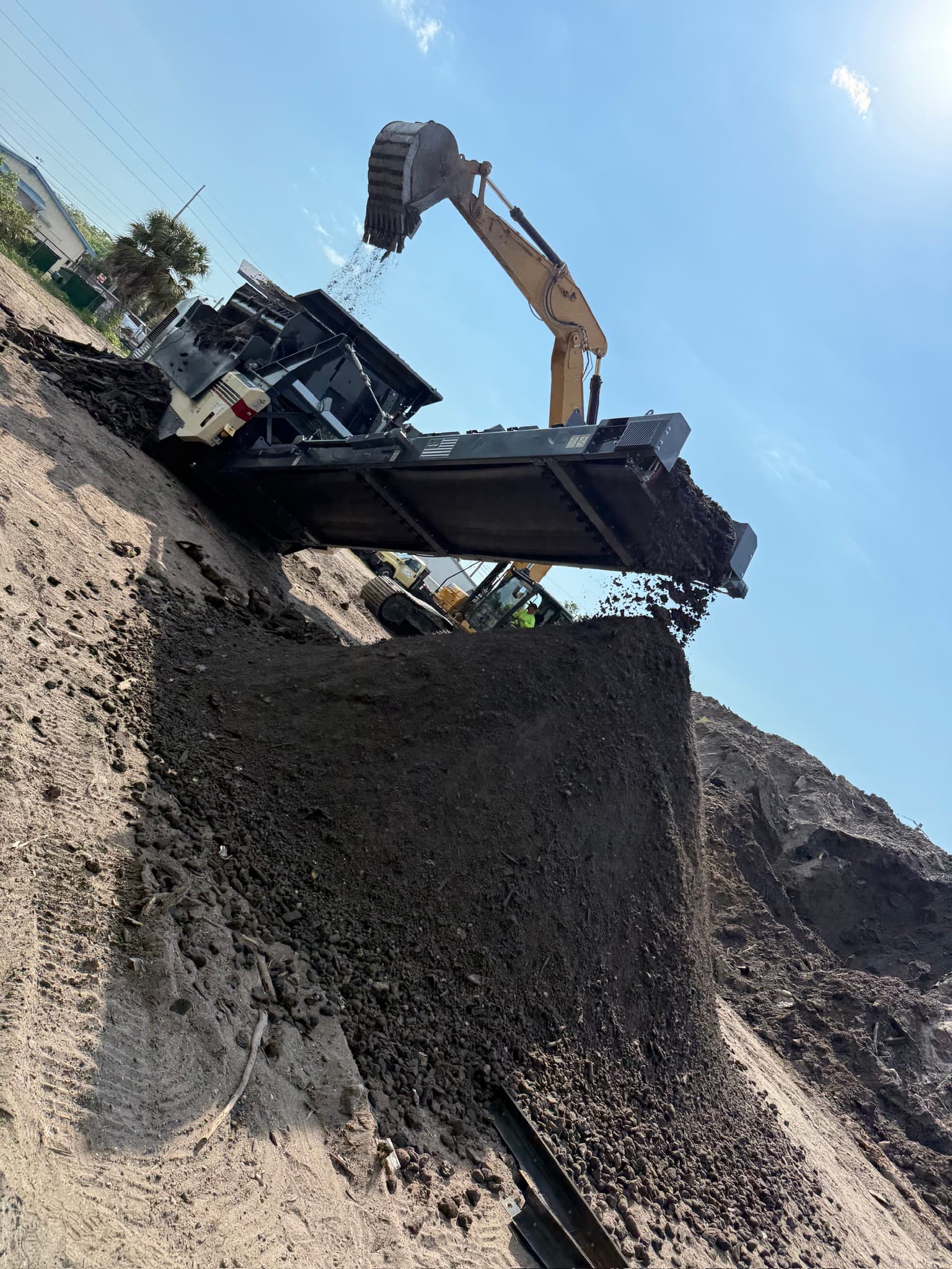 Crew compacting and preparing soil beside excavation equipment